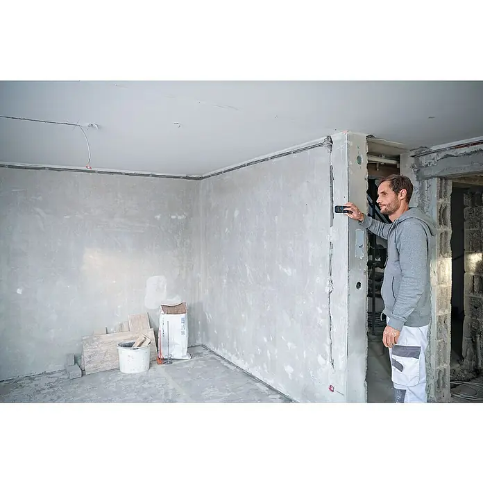 Bosch Professional Laserentfernungsmesser GLM 50-22 - Messbereich: 0,05 - 50 m - Ein Handwerker nivelliert eine frisch verputzte Wand mit einem kleinen Nivelliergerät. Der Raum ist im Rohbau.