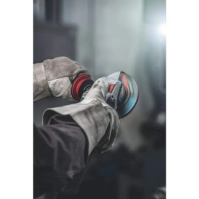 Metabo Elektro-Winkelschleifer WEV 11-125 Quick - 1.100 W, Durchmesser Scheibe: 125 mm, Leerlaufdrehzahl: 2.800 U/min - 10.500 U/min - Nahaufnahme einer Person, die mit Handschuhen einen Winkelschleifer bedient. Die Schleifscheibe ist in Bewegung und erzeugt einen Farbwischeffekt.
