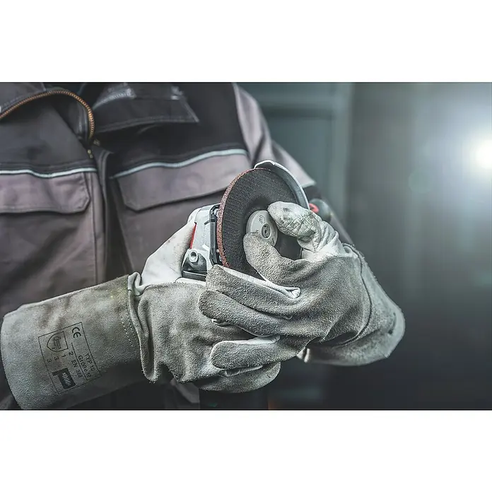 Metabo Elektro-Winkelschleifer WEV 11-125 Quick - 1.100 W, Durchmesser Scheibe: 125 mm, Leerlaufdrehzahl: 2.800 U/min - 10.500 U/min - Nahaufnahme einer Person, die mit Schutzhandschuhen einen Winkelschleifer bedient. Konzentration auf das Werkzeug und die Schutzausrüstung.