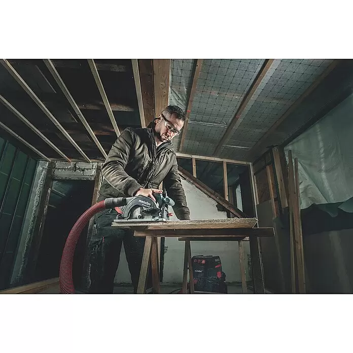Metabo CAS 18V Akku-Handkreissäge KS 18 LTX 57 - 18 V, Ohne Akku, 4.600 U/min - Ein Mann sägt mit einer Metabo KS 18 LTX 57 Handkreissäge mit rotem Absaugschlauch Holz auf einem Sägebock auf einer Baustelle.