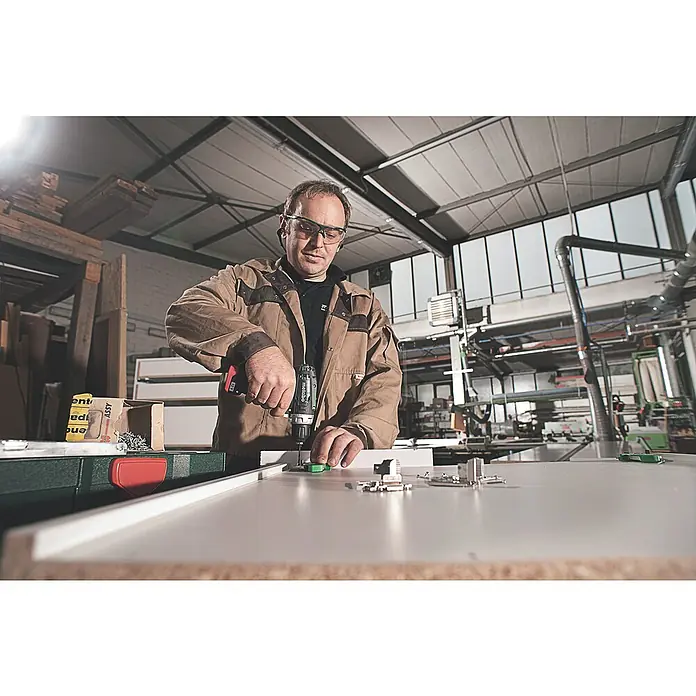 Metabo Akku-Bohrschrauber PowerMaxx BS Basic Set12 V, 2 Akkus, 2 Ah - Ein Mann benutzt einen Metabo Akku-Bohrschrauber, um Beschläge an einem weißen Schrank zu befestigen. Er trägt dabei eine Schutzbrille.