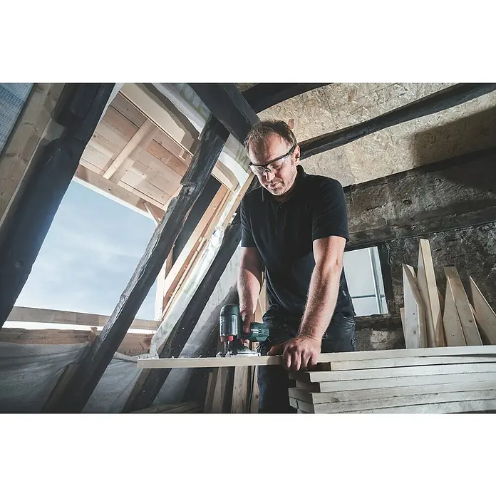 Metabo Elektro-Pendelhubstichsäge STE 100 Quick - 1.000 /min - 3.100 /min, Max. Schnitttiefe in Holz: 100 mm, Anzahl Pendelhubstufen: 4 Stk. - Ein Handwerker benutzt eine Metabo Oberfräse in einem Dachgeschoss, um Holz zu bearbeiten, wobei er eine Schutzbrille trägt.