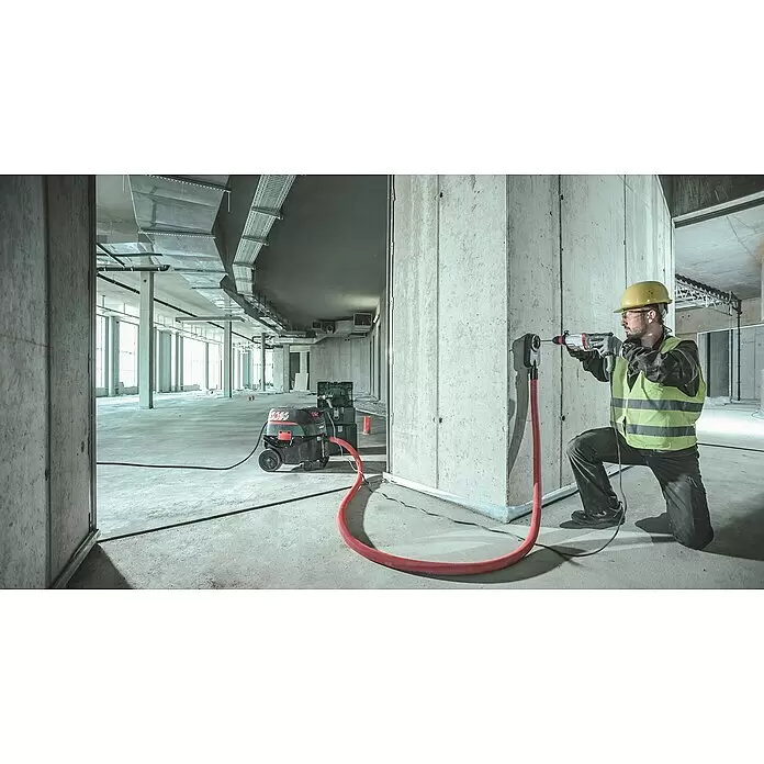 Metabo Martillo combinado UHE 2860-2 Quick - 1.100 W, 3,4 J, Alojamiento SDS-Plus - Trabajador taladra una pared de hormigón con un taladro, un accesorio de extracción de polvo y una aspiradora.