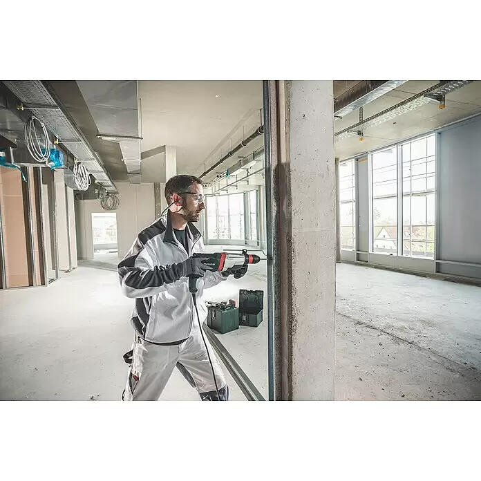 Metabo Martillo combinado 2860 Quick Set - 880 W, 3,2 J, Alojamiento SDS-Plus - Hombre con equipo de seguridad perforando un pilar de hormigón con un taladro percutor Metabo rojo y negro.