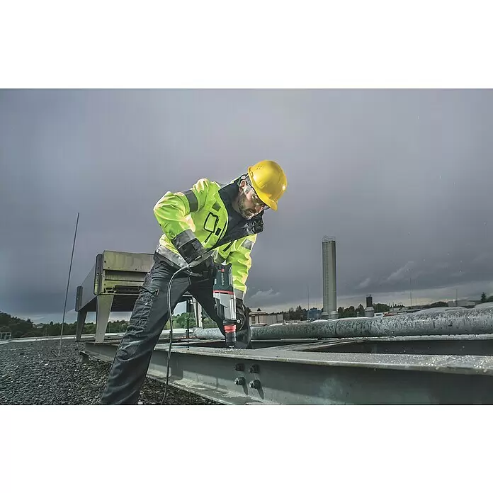 Metabo Martillo combinado 2860 Quick Set - 880 W, 3,2 J, Alojamiento SDS-Plus - Un trabajador con casco amarillo y chaqueta de seguridad taladra una viga metálica con un taladro Metabo.
