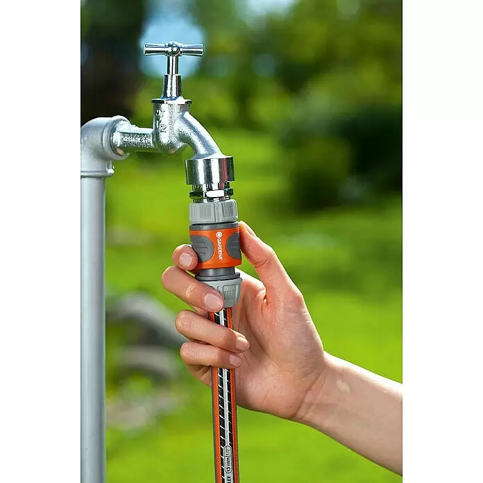 Gardena Hahnverbinder - M 22 x 1 - Hand verbindet orange-grauen Gardena Schlauchanschluss mit silbernem Gartenwasserhahn.