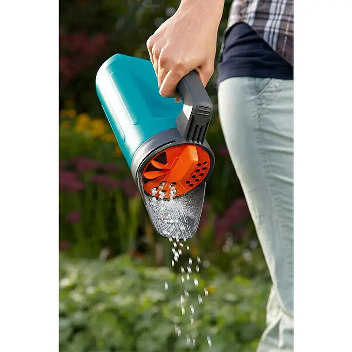 Gardena Handstreuer S - Kunststoff, Mengenregulierung - Nahaufnahme eines Gardena Streuwagens in Aktion, der Dünger über einem Garten verteilt. Die Streufunktion ist deutlich sichtbar.