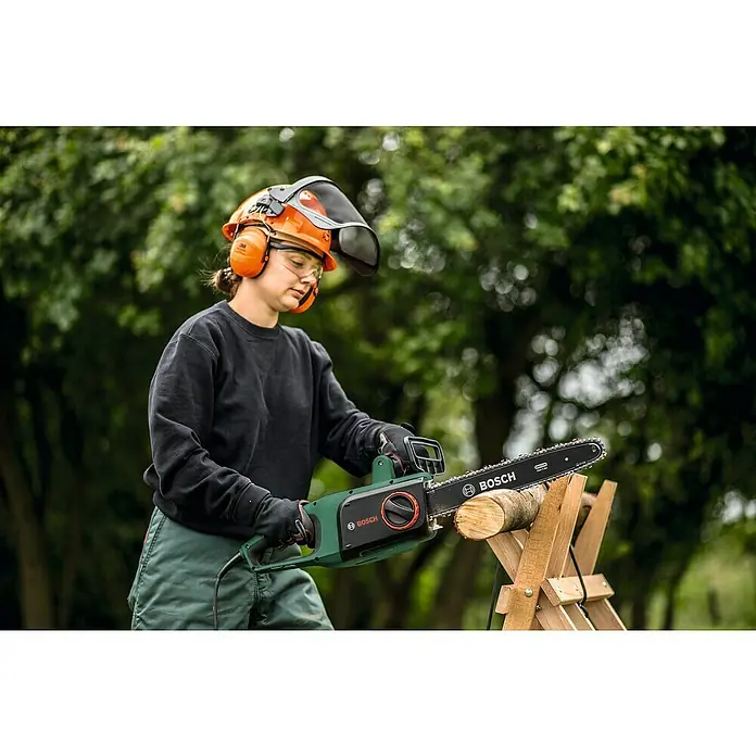 Bosch Motosierra eléctrica Universal Chain 35 - 1.800 W, Longitud de la cuchilla: 35 cm - Una mujer opera una motosierra Bosch para cortar un tronco, usando equipo de seguridad al aire libre.