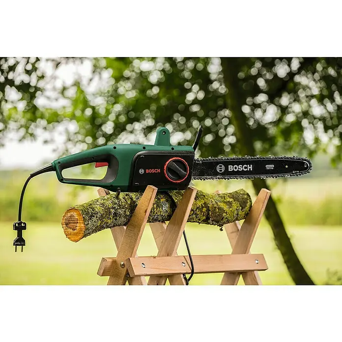 Bosch Motosierra eléctrica Universal Chain 35 - 1.800 W, Longitud de la cuchilla: 35 cm - Una motosierra Bosch verde sobre un caballete de troncos con un fondo verde. La motosierra está conectada con un cable de alimentación negro.