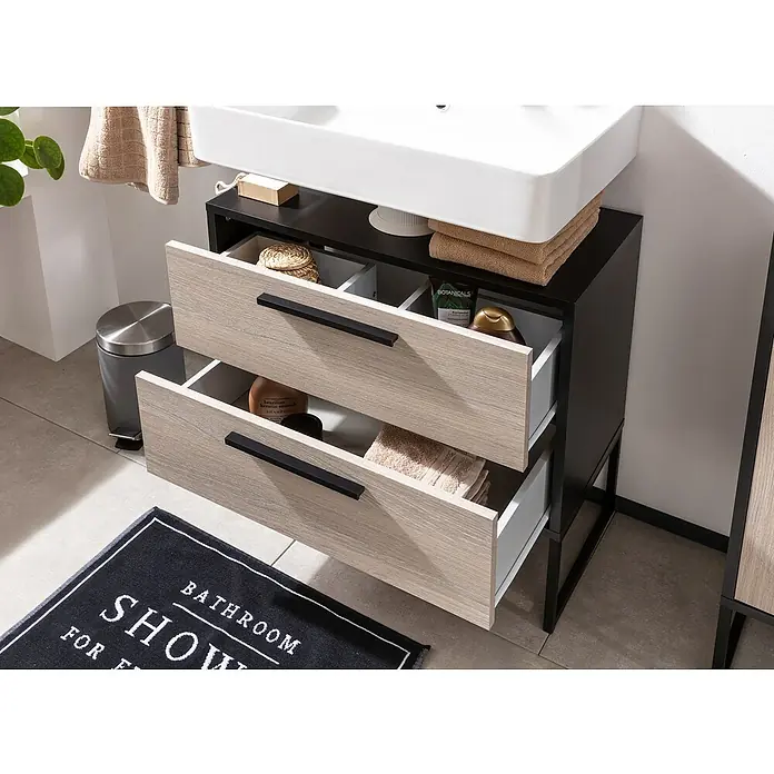 BAUHAUS Jannik Badmöbel-Set - Gesamtbreite Badmöbel: 65 cm, Steinesche/Anthrazit, Matt, Mit Midischrank, 5 -tlg. - Ein Waschtischunterschrank mit zwei offenen Schubladen, gefüllt mit Badartikeln und Handtüchern, unter einem weißen Waschbecken.