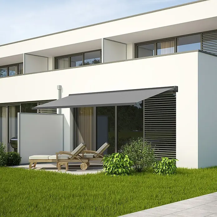 SmartSun Toldo con motor WiFi Dark Fiji II - Antracita, Ancho: 2,95 m, Caída: 2 m - Un elegante toldo gris proporciona sombra en un patio con tumbonas frente a un moderno edificio residencial.