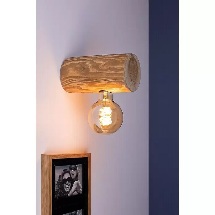 Spotlight Wandleuchte Trabo Simple - 25 W, L x B x H: 20 x 8 x 8 cm, Gebeizte Kiefer, E27 - Rustikale Wandlampe aus Holz mit einer bernsteinfarbenen Edison-Glühbirne, die eine helle Wand und einen Bilderrahmen warm beleuchtet.
