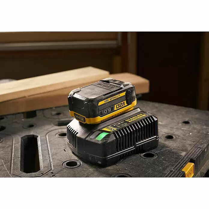 Stanley FatMax Akku SFMCB206-XJ - 18 V, 6 Ah - Schwarzer und gelber Stanley FatMax V20 Lithium-Ionen-Akku lädt auf einem schwarzen Ladegerät auf einer Werkbank, mit Holz im Hintergrund.