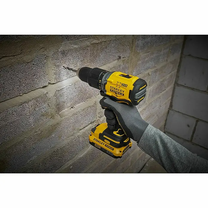 Stanley FatMax Akku-Schlagbohrschrauber SFMCD715D2K-QW - 18 V, 2 Akkus, 60 Nm - Nahaufnahme eines Stanley Fatmax Akku-Bohrers beim Bohren in eine Ziegelwand, der Akku ist gut sichtbar.