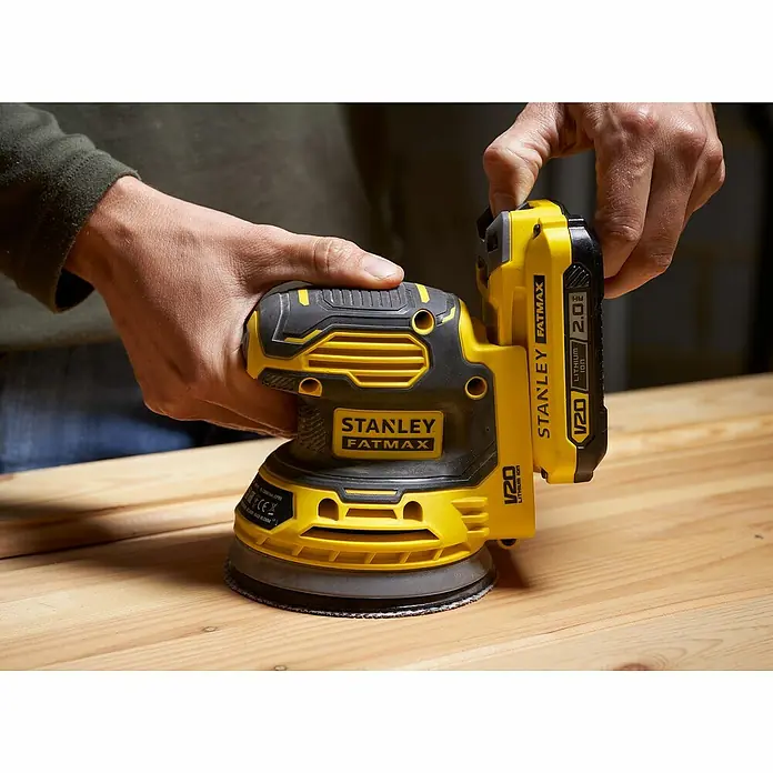 Stanley FatMax Akku-Exzenterschleifer SFMCW220D1S-QW18 V, 1 Akku, Durchmesser Schleifteller: 125 mm - Nahaufnahme eines Akku-Exzenterschleifers STANLEY FATMAX V20, der auf einem Holztisch verwendet wird.