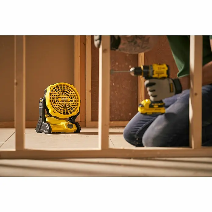 Stanley FatMax Akku-Ventilator SFMCE001B-XJ - 18 V, Ohne Akku, Luftmenge: 1.100 m³/h - Gelber Stanley-Ventilator steht auf dem Boden, während eine Person eine Bohrmaschine benutzt.