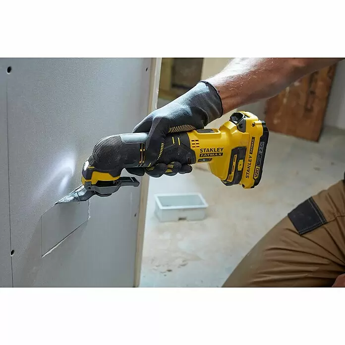 Stanley FatMax Akku-Multifunktionswerkzeug SFMCE500D2K-QW - 18 V, 2 Akkus, 2 Ah - Eine behandschuhte Hand verwendet ein gelb-schwarzes Stanley FatMax Akku-Multifunktionswerkzeug, um Trockenbauwände zu schneiden, mit Licht auf den Schnittbereich.