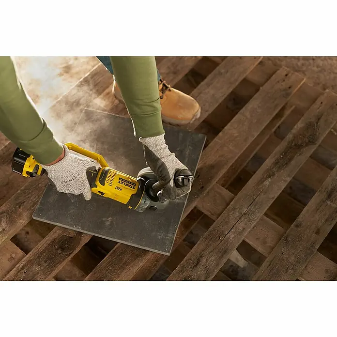 Stanley FatMax Akku-Winkelschleifer SFMCG400B-XJ - Ohne Akku, Durchmesser Scheibe: 125 mm, 9.000 U/min - Eine Person schneidet mit einem gelben Stanley FATMAX V20 Winkelschleifer eine Fliese, wobei Staub aufwirbelt.