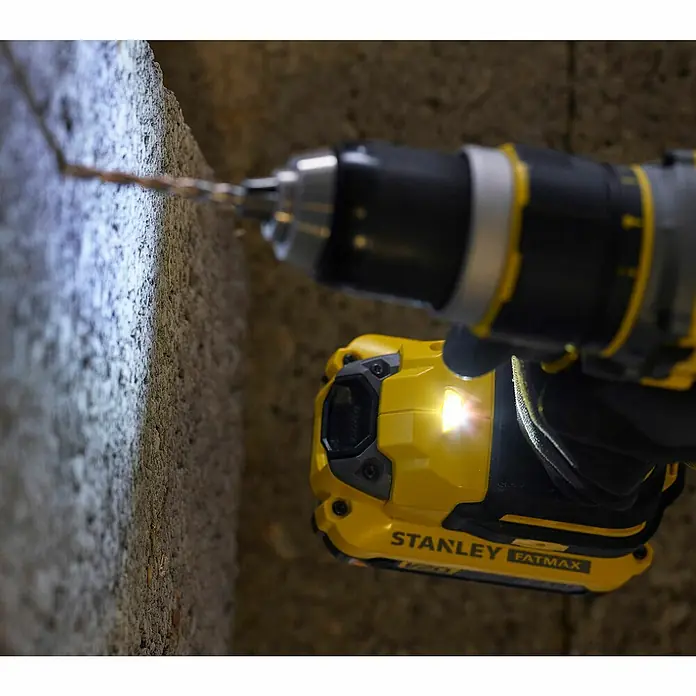 Stanley FatMax Akku-Schlagbohrschrauber SFMCD721B-XJ - 18 V, Ohne Akku, 80 Nm - Nahaufnahme eines Stanley Fatmax Akku-Bohrers beim Bohren in eine Wand, wobei der integrierte Scheinwerfer das Arbeitsfeld beleuchtet.
