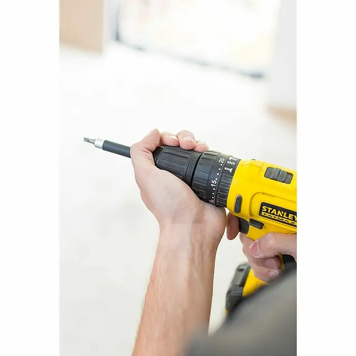 Stanley FatMax Akku-Schlagbohrschrauber FMC021S2-QW - 10,8 V, 2 Akkus, 1,5 Ah, 27 Nm - Nahaufnahme eines gelben Stanley Fatmax Akku-Bohrschraubers, der von Händen gehalten wird, mit Blick auf das Bohrfutter und Drehmomenteinstellungen.