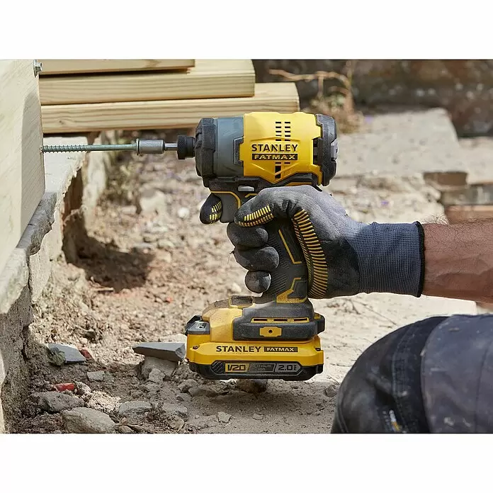 Stanley FatMax Akku-Schlagschrauber SFMCF810D2K-QW - 18 V, 2 Akkus, 2 Ah, 170 Nm - Eine Person in Arbeitshandschuhen hält einen gelb-schwarzen Stanley FatMax Schlagschrauber, der eine lange Schraube in einen Holzbalken treibt.