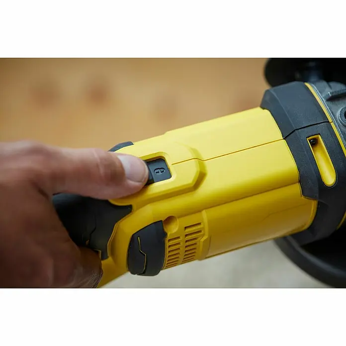 Stanley FatMax Akku-Winkelschleifer SFMCG400M2K-QW - 2 Akkus, 4 Ah, Durchmesser Scheibe: 125 mm, 9.000 U/min - Nahaufnahme eines gelben Winkelschleifers, bei dem ein Finger den Entriegelungsknopf drückt, um die Sicherheit des Geräts zu gewährleisten.