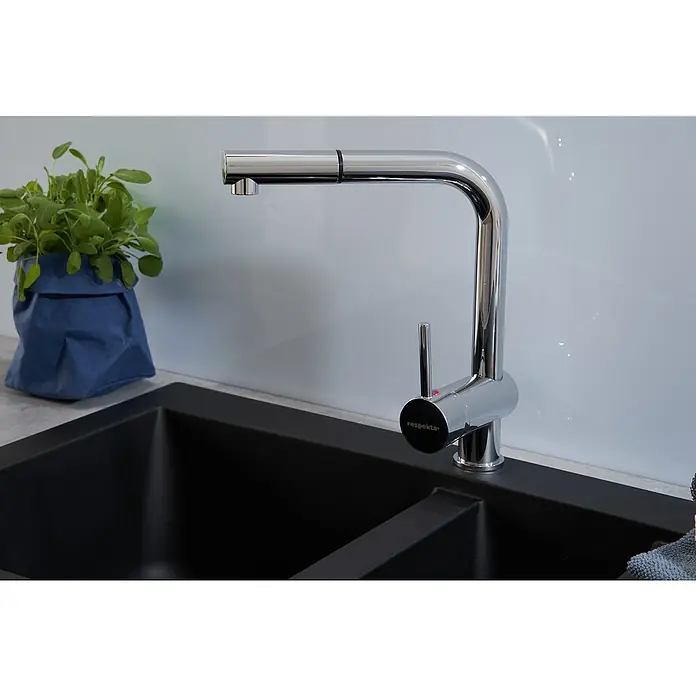 Respekta Einbauspüle Denver - 50 x 100 cm, Anzahl Becken: 1,5 Stk., Schwarz - Ein chromfarbener Respekta Küchenarmatur mit Ausziehbrause über einer schwarzen Spüle, daneben ein Kräutertopf in einer blauen Papiertüte.