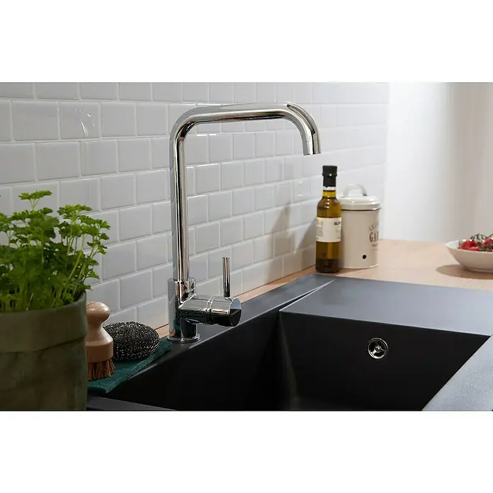 Respekta Einbauspüle Denver - 86 x 50 cm, Schwarz, Anzahl Becken: 1 Stk. - Eine moderne Küchenarmatur aus Chrom steht auf einer dunklen Spüle, umgeben von Kräutern, einer Bürste und Küchenutensilien.