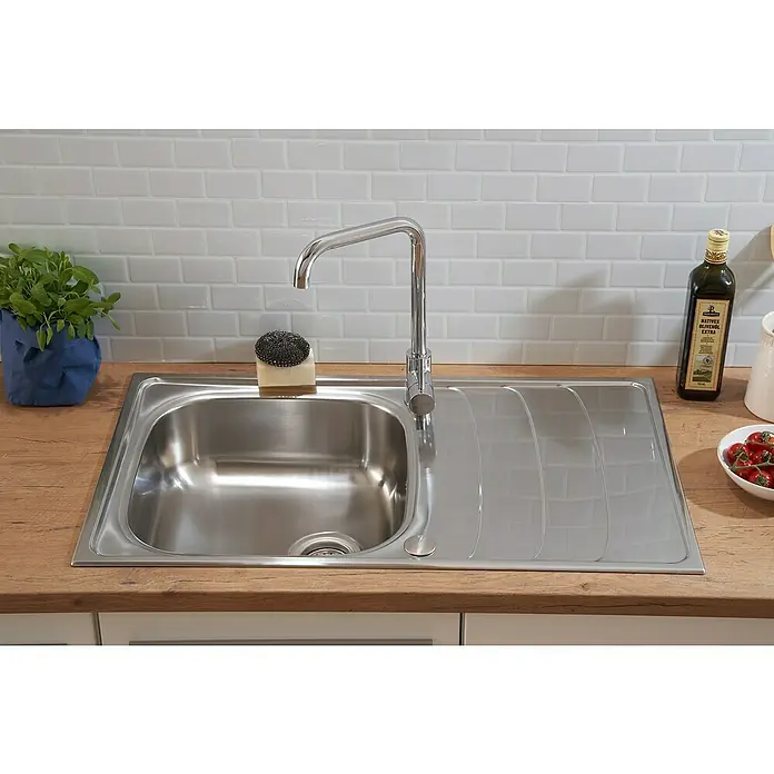 Respekta Einbauspüle Miami - 86 x 50 cm, Edelstahl - Nahaufnahme einer Edelstahlspüle mit Abtropffläche, Armatur, Spülschwamm, Pflanze, Olivenöl und Tomaten. Ideal für die moderne Küche.
