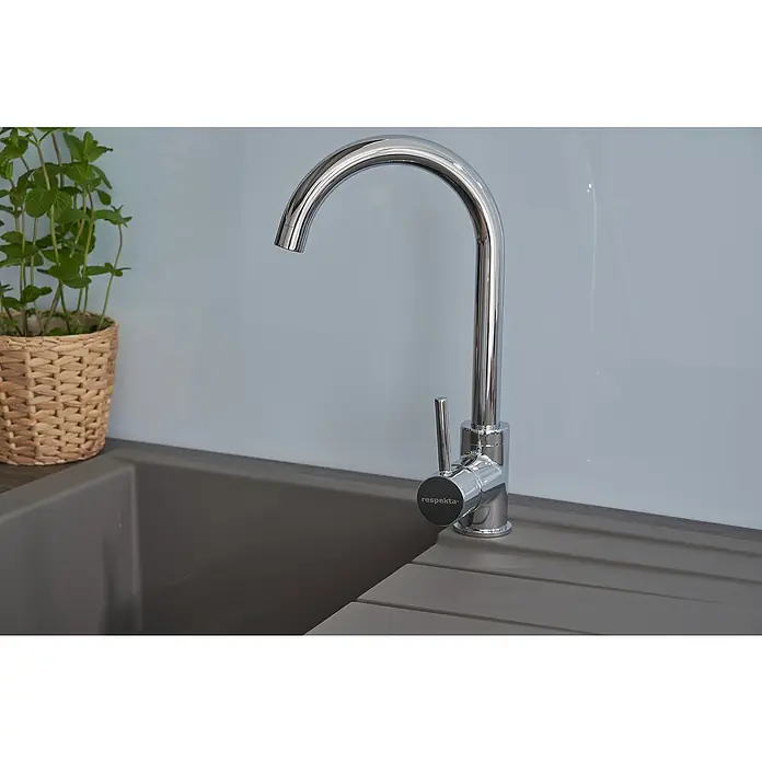 Respekta Einbauspüle Houston - 80 x 50 cm, Grau, Anzahl Becken: 1 Stk. - Nahaufnahme eines RESPEKTA Wasserhahns aus glänzendem Chrom, der auf einer grauen Spüle montiert ist, mit einer Topfpflanze im Hintergrund.