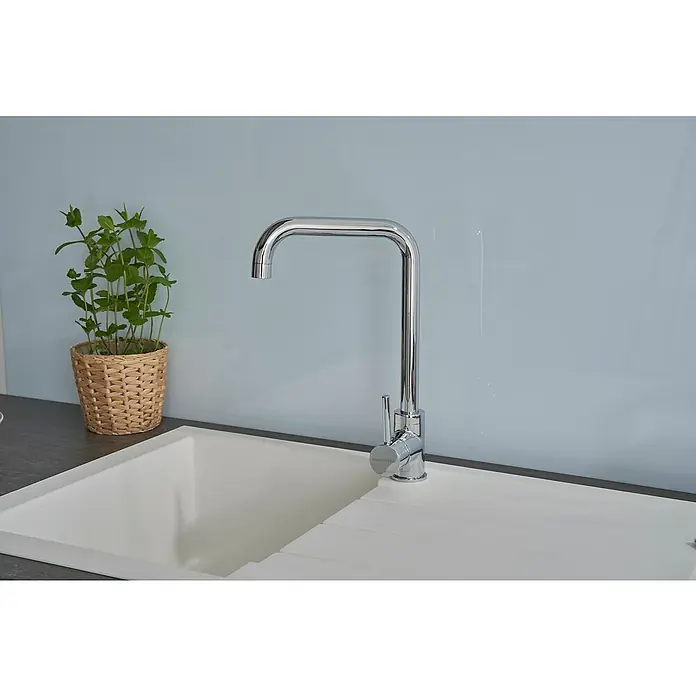 Respekta Einbauspüle Houston - 80 x 50 cm, Weiß, Anzahl Becken: 1 Stk. - Nahaufnahme einer modernen Küchenarmatur aus Chrom über einer Spüle, neben einem Topf mit grüner Pflanze, vor einem blauen Hintergrund.