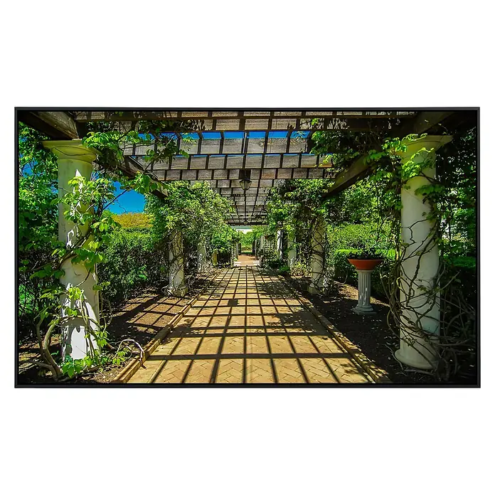 Papermoon Infrarot-Bildheizkörper Garten Gehweg - 60 cm x 500 mm, 350 W - Ein malerischer Gartenweg mit einer Pergola, die von üppigem Grün und Säulen gesäumt ist. Das Sonnenlicht erzeugt interessante Schattenmuster.
