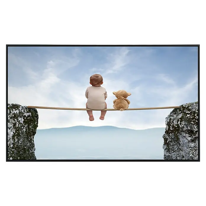 Papermoon Infrarot-Bildheizkörper Babyspiele - 90 x 50 cm, 450 W - Ein Baby und ein Teddy sitzen auf einem Steg zwischen zwei Felsen unter einem bewölkten Himmel. Die Szene wirkt friedlich und nachdenklich.