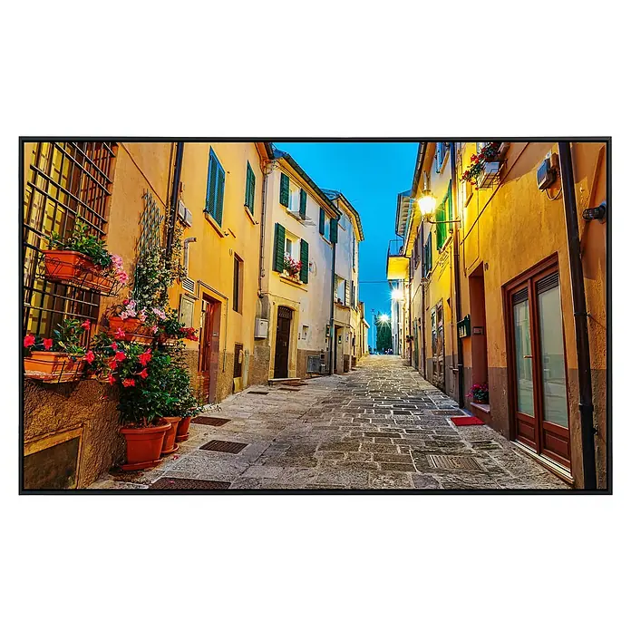 Papermoon Infrarot-Bildheizkörper Altstadt in Italien - 90 x 50 cm, 450 W - Die fotorealistische Leinwand zeigt eine belebte Gasse in einer italienischen Stadt mit farbenfrohen Gebäuden und blühenden Blumenkästen.