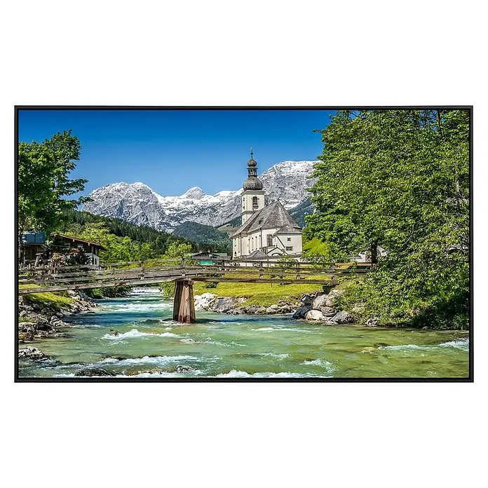 Papermoon Infrarot-Bildheizkörper Bayerische Alpen - 120 x 60 cm, 1.000 W - Die Ramsauer Kirche St. Sebastian vor schneebedeckten Bergen, mit einer Holzbrücke über einen Fluss, präsentiert eine malerische Landschaft.