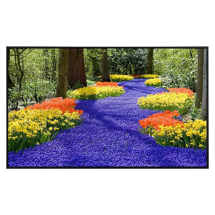 Papermoon Infrarot-Bildheizkörper Frühlingsblumen 2 - 100 cm x 600 mm, 600 W - Farbenfrohes Blumenbeet mit blauen, gelben und orangefarbenen Tulpen zwischen hohen Bäumen, das einen bunten Gartenweg bildet.