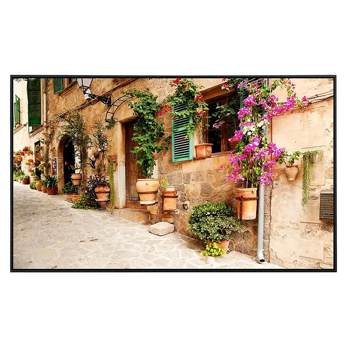 Papermoon Infrarot-Bildheizkörper Valdemossa Mallorca - 100 x 60 cm, 800 W - Einladende Gasse mit blühenden Pflanzen in Terrakottatöpfen vor einem Haus mit grünen Fensterläden, die eine malerische Szene schaffen.