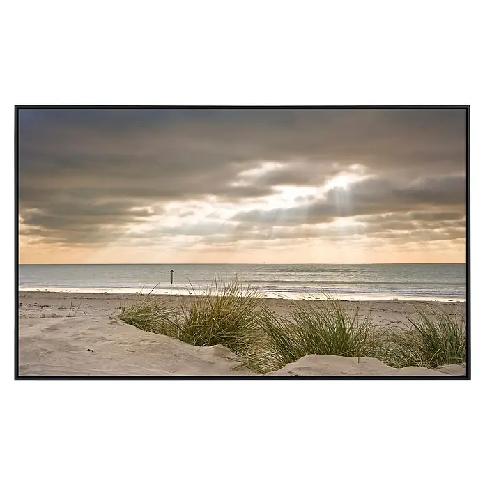 Papermoon Infrarot-Bildheizkörper Dünen im Winter - 120 x 60 cm, 1.200 W - Atmosphärische Küstenaufnahme mit Sanddünen, sanften Wellen und strahlenden Sonnenstrahlen durch die Wolken, gerahmt in elegantem Schwarz.