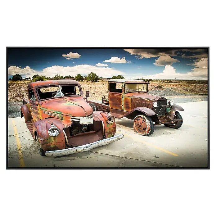 Papermoon Infrarot-Bildheizkörper Verlassene alte Autos - 90 x 50 cm, 450 W - Zwei verrostete Oldtimer-Trucks stehen auf einem Parkplatz, die Farbe ist abgeblättert, was ihren Vintage-Charme unter einem bewölkten Himmel noch verstärkt.