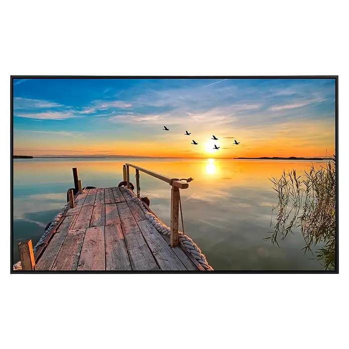 Papermoon Infrarot-Bildheizkörper Sunset Pier - 60 x 50 cm, 350 W - Sonnenuntergang über einem See, gesehen von einem hölzernen Pier, mit Vögeln im Himmel, eingefasst in einem schwarzen Rahmen.