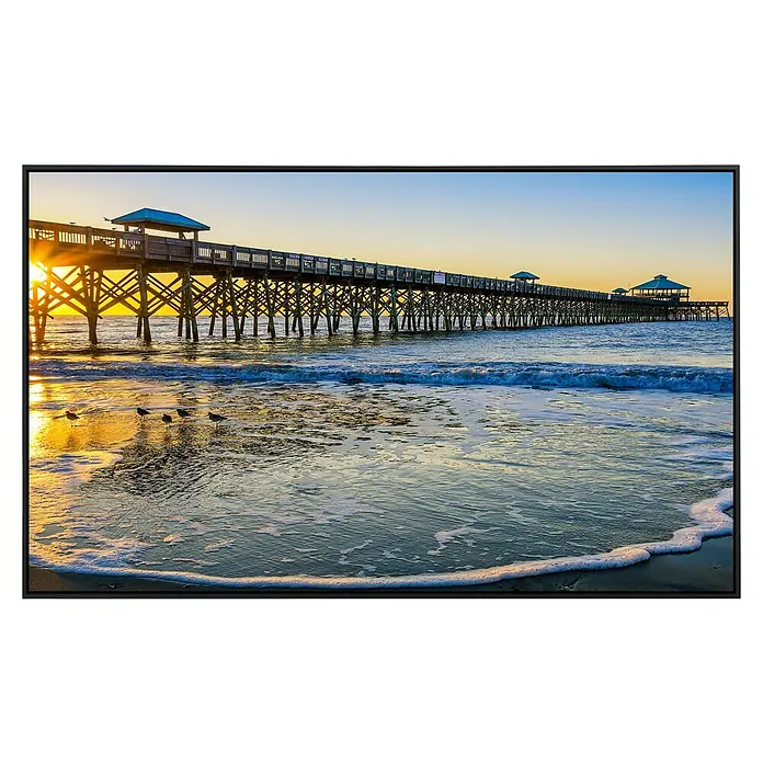 Papermoon Infrarot-Bildheizkörper Torheit Pier Winter Sonnenaufgang - 120 x 60 cm, 1.000 W - Ein langer Steg erstreckt sich über das Meer, während die untergehende Sonne goldenes Licht wirft. Wellen umspülen den Strand mit einigen Vögeln.