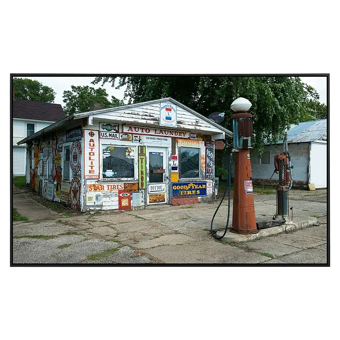 Papermoon Infrarot-Bildheizkörper Alte Vintage Retro Tankstelle - 100 x 60 cm, 800 W - Das Bild zeigt eine skurrile "Auto Laundry" mit einer eklektischen Sammlung von Oldtimer-Schildern und Zapfsäulen.