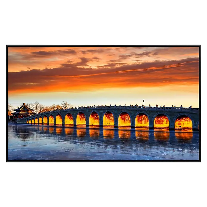 Papermoon Infrarot-Bildheizkörper Beijing Summer Palace Bridge - 90 x 50 cm, 450 W - Abendliche Ansicht einer alten Steinbrücke mit beleuchteten Bögen und sich spiegelndem Wasser unter einem orangefarbenen Himmel.