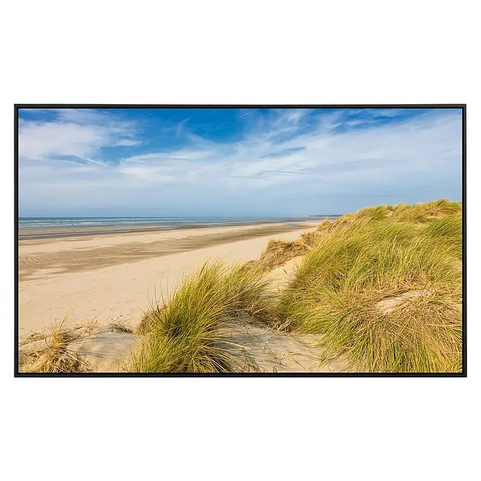 Papermoon Infrarot-Bildheizkörper Dunes Touquet - 90 x 50 cm, 450 W - Ein gerahmtes Bild mit Dünenlandschaft, die sich bis zum Strand und Meer erstreckt, unter einem strahlend blauen Himmel.