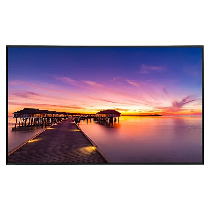 Papermoon Infrarot-Bildheizkörper Sunset Pier Malediven120 x 60 cm, 750 W - Die TV-Ansicht zeigt einen Holzsteg zu Hütten über dem Wasser bei Sonnenuntergang mit lebendigen Farben und einem ruhigen Meer.
