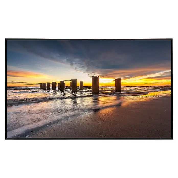 Papermoon Infrarot-Bildheizkörper Panorama Sonnenuntergang Indonesien - 100 x 60 cm, 600 W - Das Kunstwerk zeigt Pfähle im Meer bei Sonnenuntergang, gerahmt in einem eleganten, schwarzen Rahmen, der die warmen Farben hervorhebt.