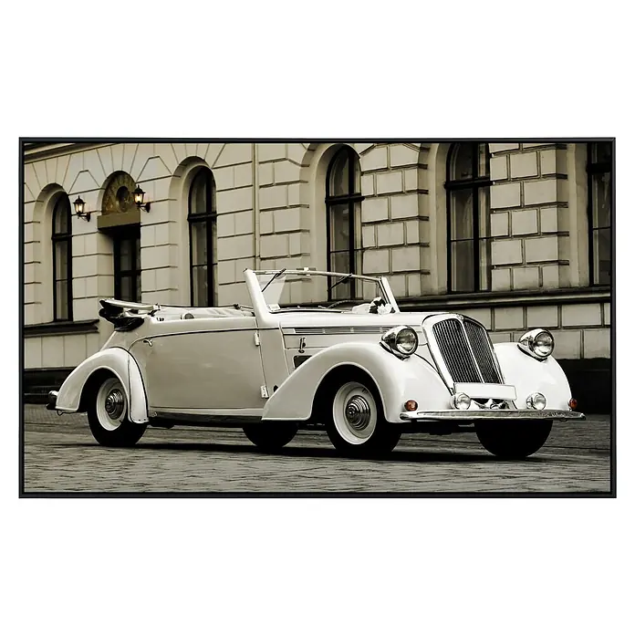 Papermoon Infrarot-Bildheizkörper 1938 Steyr Modell 120 - 60 x 50 cm, 350 W - Ein elegantes, klassisches weißes Cabriolet, abgestellt vor einem Gebäude mit auffälliger Architektur, das den zeitlosen Stil des Fahrzeugs betont.