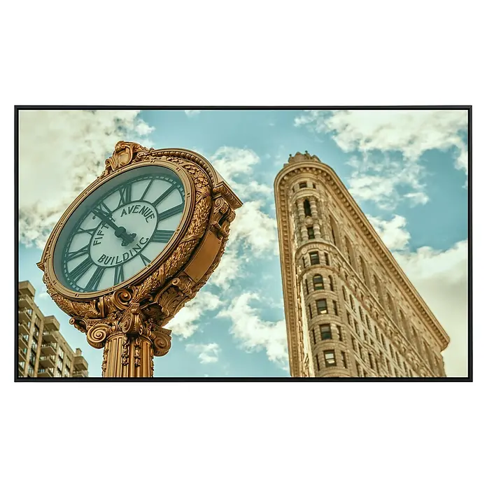 Papermoon Infrarot-Bildheizkörper Flatiron New York - 120 x 60 cm, 1.000 W - Detailaufnahme einer goldenen Uhr vor dem Flatiron Building, New York, unter blauem Himmel.