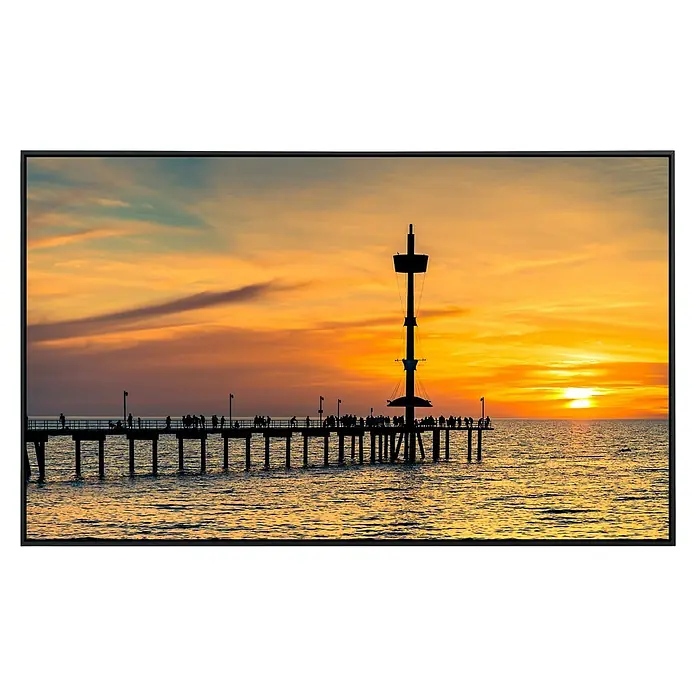 Papermoon Infrarot-Bildheizkörper Brighton Steg - 60 x 50 cm, 350 W - Silhouette eines Piers und Turms bei Sonnenuntergang, die ruhige Reflexionen auf dem Wasser erzeugen und eine friedliche Atmosphäre schaffen.