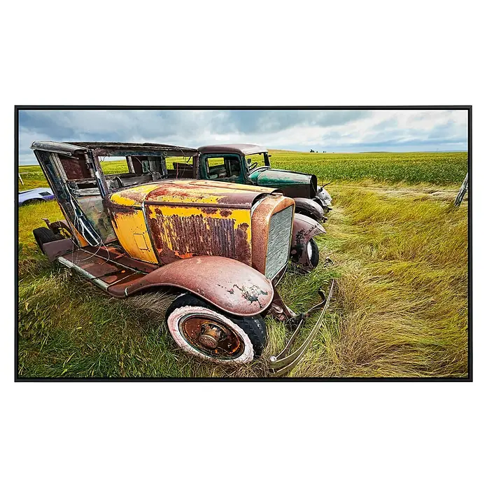 Papermoon Infrarot-Bildheizkörper Oldtimer 2 - 60 x 50 cm, 350 W - Verrostete Oldtimer-Autos stehen auf einem Feld mit Gras. Das gelbe Auto im Vordergrund ist stark verfallen, daneben ein grünes Modell.